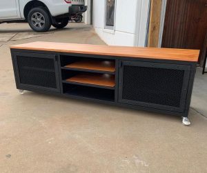 Mueble de TV industrial con superficie de madera, estructura metálica negra, puertas con malla, y ruedas en la base. Atractivo y funcional para almacenamiento en salones modernos.