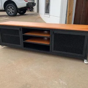 Mueble de TV industrial con superficie de madera, estructura metálica negra, puertas con malla, y ruedas en la base. Atractivo y funcional para almacenamiento en salones modernos.