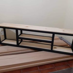 Mueble de TV moderno con estructura de metal negro y estantes de madera clara. Diseño minimalista con dos niveles para almacenamiento. Ideal para salas contemporáneas.