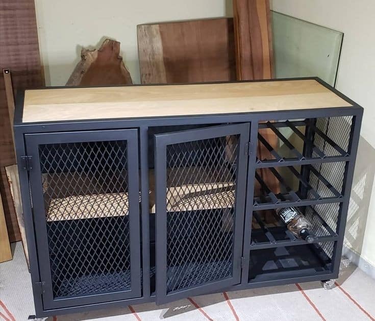 Gabinete industrial de metal negro con puertas de malla y parte superior de madera clara. Incluye estantes para botellas. Diseño funcional y moderno, ideal para almacenar vinos.