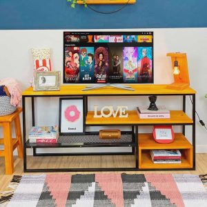 Mesa de TV moderna con estructura de metal negro y repisas de madera. Posee decoraciones eclécticas, con espacio para almacenamiento, ideal para un salón contemporáneo.