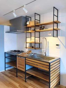 Cocina moderna con mueble de madera y metal, que incluye estantes abiertos, fregadero de acero inoxidable, encimera con quemadores y campana extractora integrada.