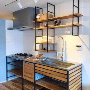 Cocina moderna con mueble de madera y metal, que incluye estantes abiertos, fregadero de acero inoxidable, encimera con quemadores y campana extractora integrada.