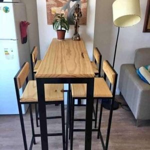 Mesa alta con estructura metálica negra y superficie de madera clara. Incluye cuatro sillas a juego con respaldo de madera y patas metálicas. Ideal para espacios modernos.