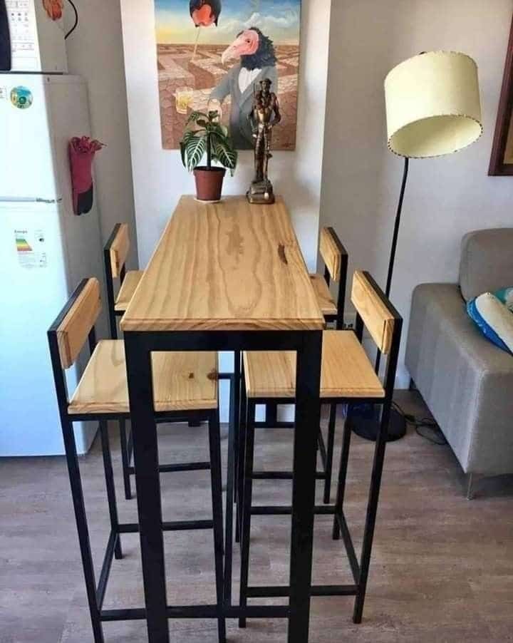 Mesa alta con estructura metálica negra y superficie de madera clara. Incluye cuatro sillas a juego con respaldo de madera y patas metálicas. Ideal para espacios modernos.