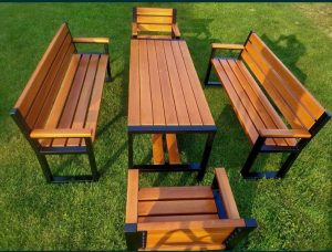 Juego de muebles de jardín: mesa rectangular de madera con estructura metálica negra, acompañada de dos bancas y dos sillas a juego, en un césped verde.