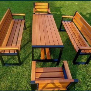 Juego de muebles de jardín: mesa rectangular de madera con estructura metálica negra, acompañada de dos bancas y dos sillas a juego, en un césped verde.