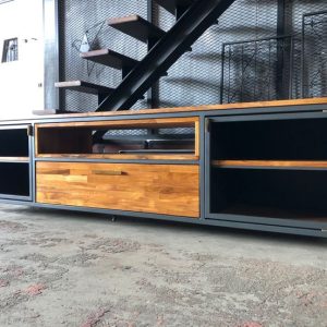 Mueble de TV industrial con estructura metálica negra y acabados de madera. Cuenta con estantes abiertos, puertas laterales y un cajón central. Diseño moderno y funcional.