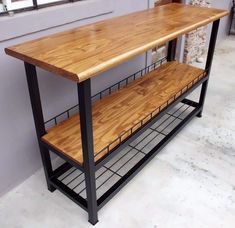 Mesa estrecha con estructura de metal negro y superficie de madera clara. Cuenta con un estante intermedio de madera y una rejilla en la base para almacenamiento adicional.