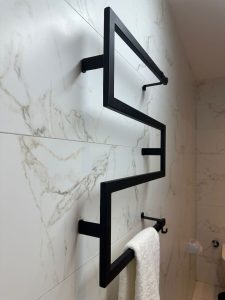 Toallero de metal negro en ángulo recto, montado en una pared de mármol blanco. Diseño minimalista y moderno, ideal para baños contemporáneos.