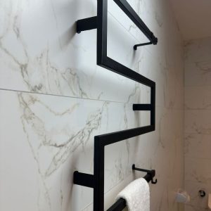 Toallero de metal negro en ángulo recto, montado en una pared de mármol blanco. Diseño minimalista y moderno, ideal para baños contemporáneos.
