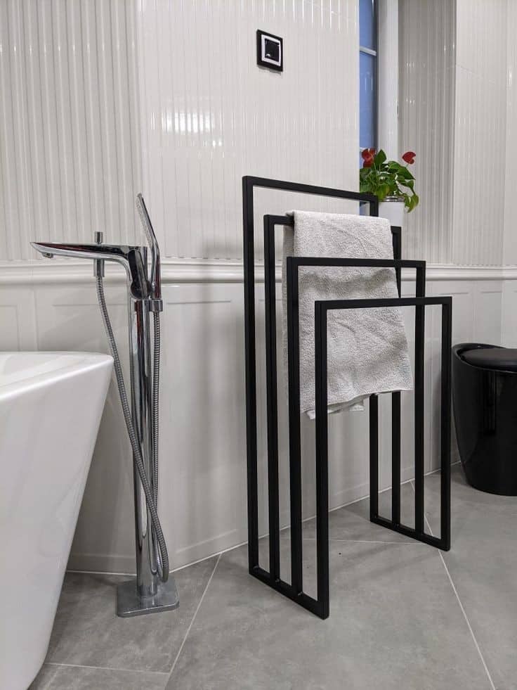 Toallero de metal negro con diseño minimalista geométrico, compuesto por tres barras de diferentes tamaños, ideal para baños modernos.